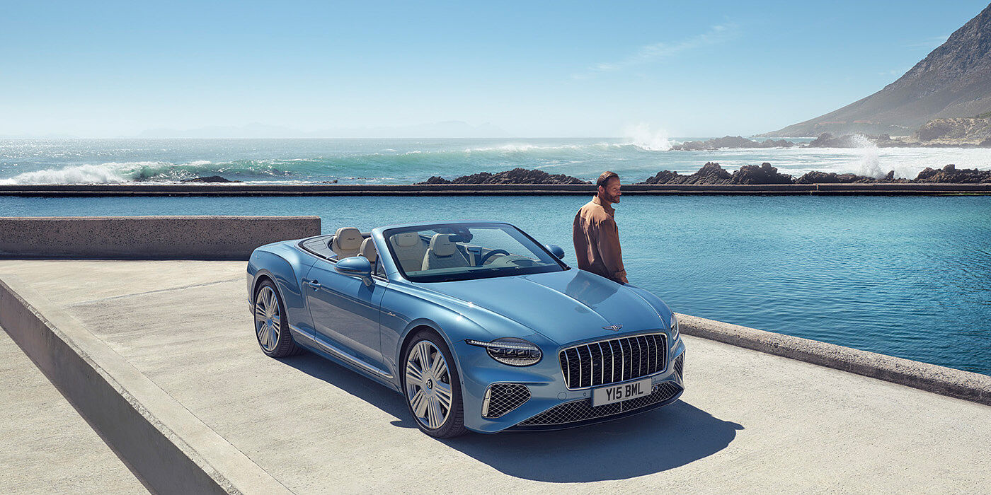 Bentley Athens New Bentley Continental GTC Azure convertible front view in Light Windsor blue paint with 22 inch ten spoke wheels parked by the sea in the sunshine