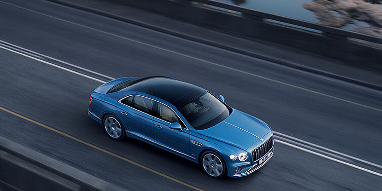 Bentley Athens New Bentley Flying Spur Azure sedan in Light windsor blue paint by Mulliner, with 22 inch Azure wheels seen from overhead driving dynamically on a country road