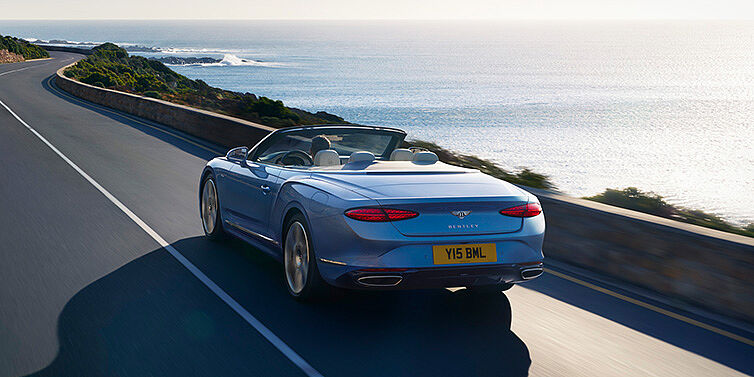 Bentley Athens New Bentley Continental GTC Azure convertible rear view in Light Windsor blue paint with 22 inch ten spoke wheels driving dynamically on an ocean road in the sunshine