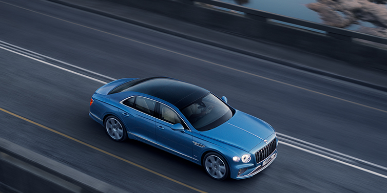 Bentley Athens Bentley Flying Spur Speed sedan side profile in Tourmaline Green paint driving dynamically on a mountain road at sunset