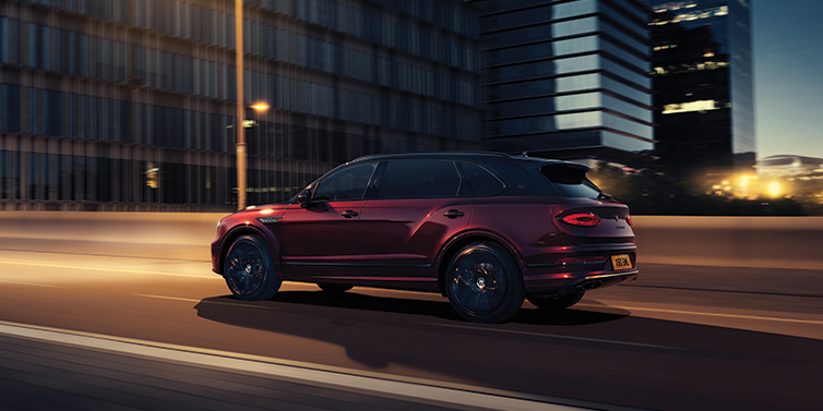 Bentley Athens Bentley Bentayga Extended Wheelbase Mulliner SUV in Cricket Ball red paint driving dynamically in city at night